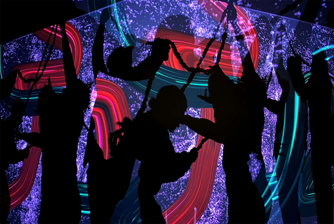Silhouettes of people interacting with an immersive, colorful digital art projection.