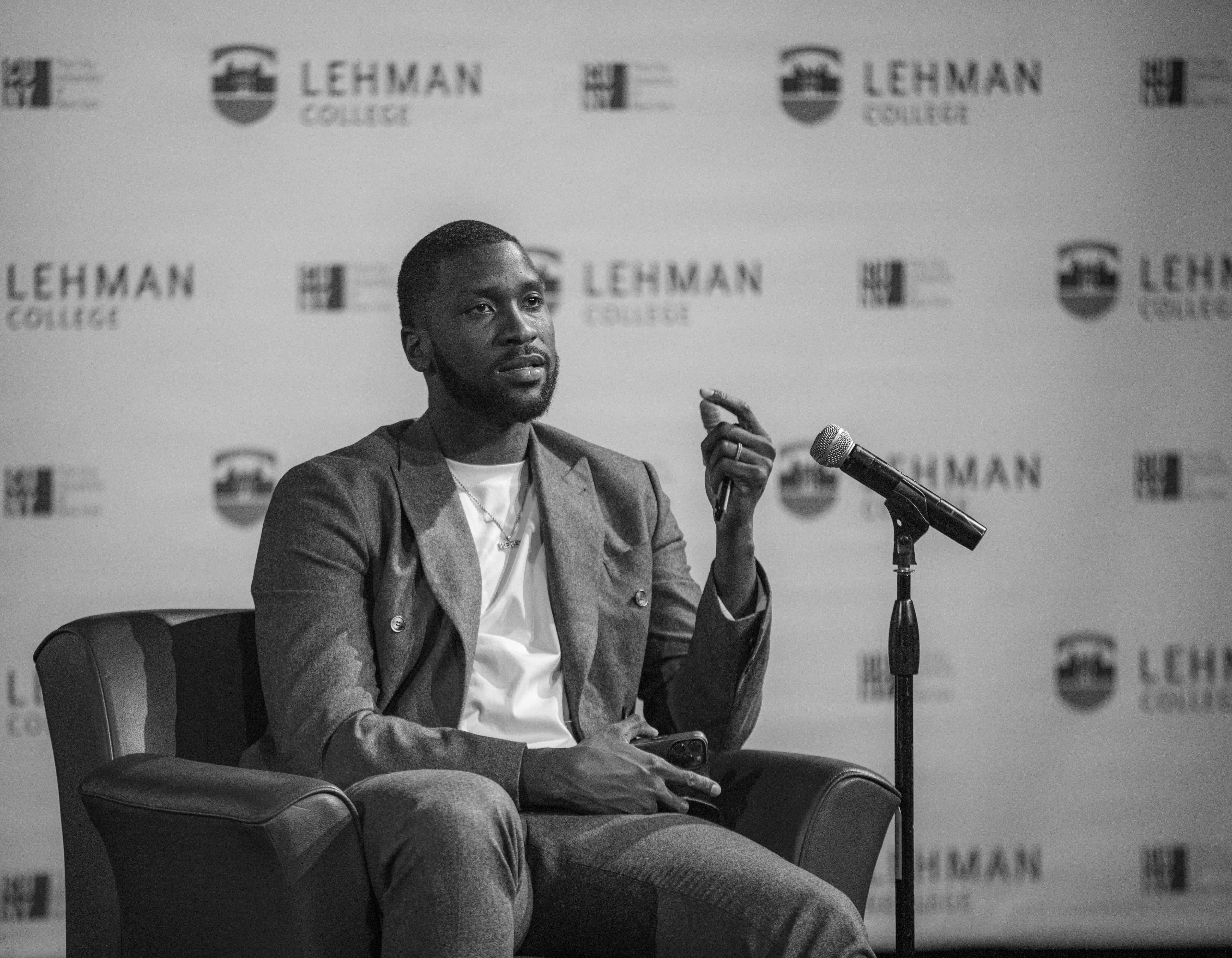 A Black man sitting down speaking in front of a microphone