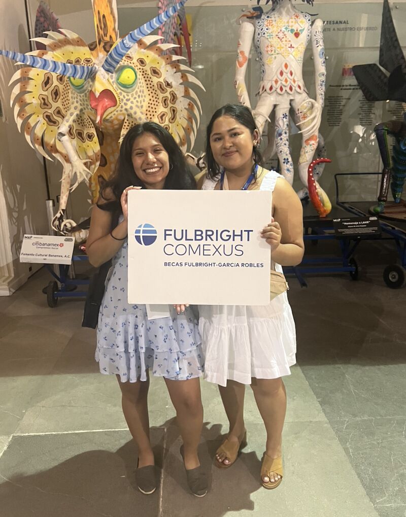 Two Hispanic women posing together with a sign reading Fulbright-COMEXUS.