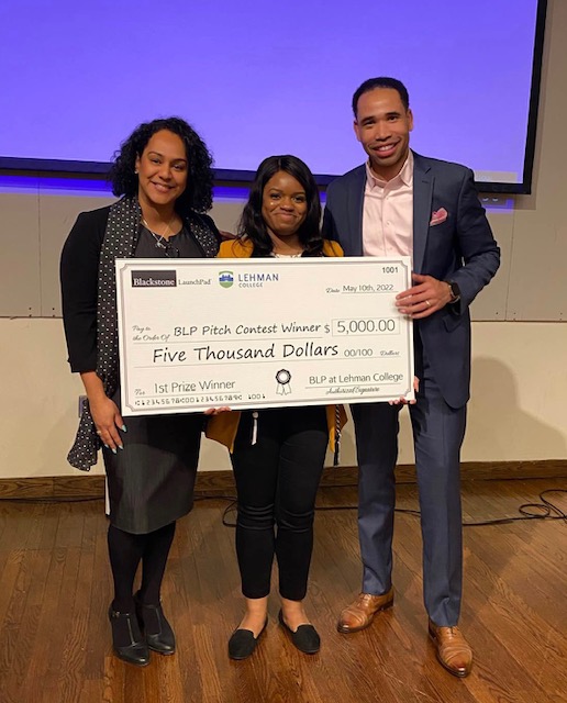 Three people face the camera, holding a giant check for five thousand dollars.