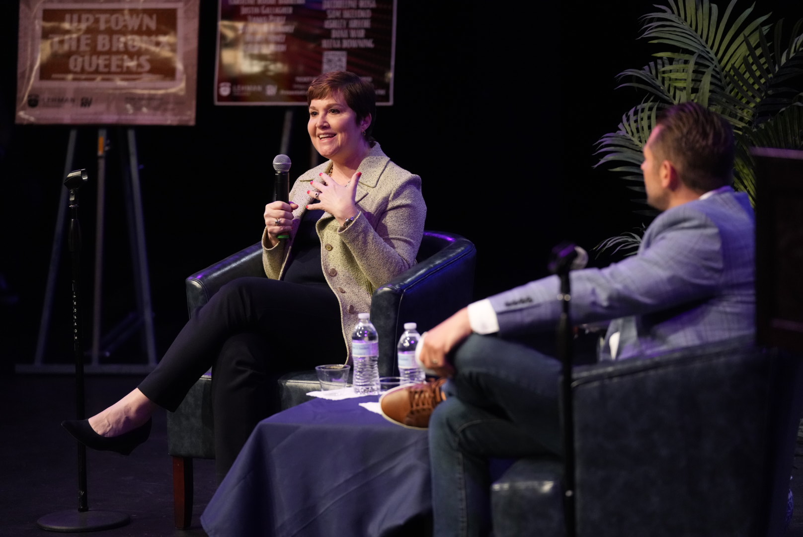 A man and a woman sitting on a stage conversing. The woman is gesturing.