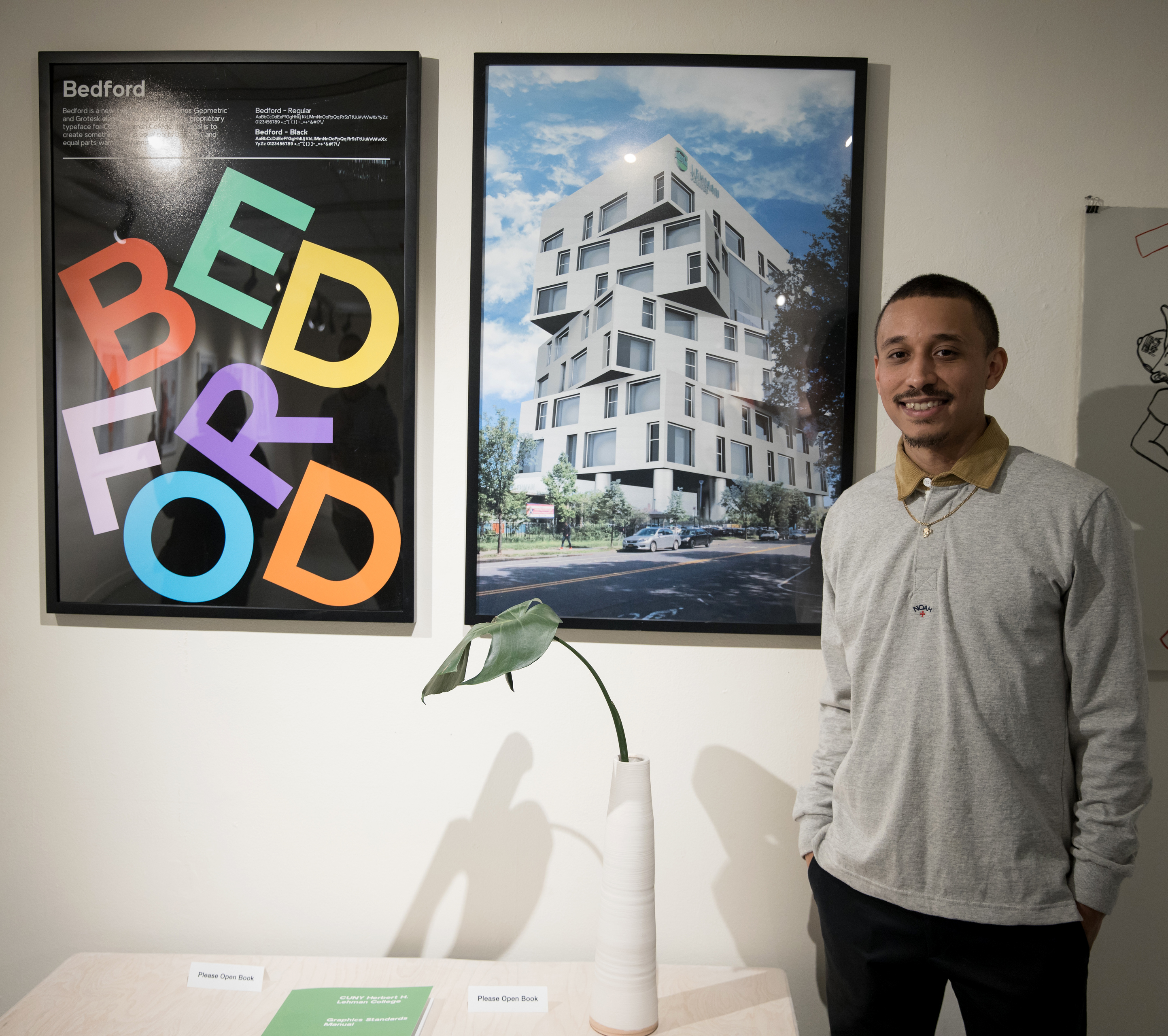 A young man stands in front of posters mounted on a wall.