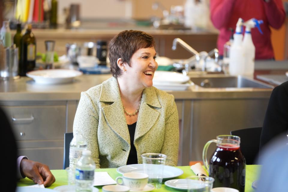 A woman with short hair is sitting at a table with a place setting in front of her.