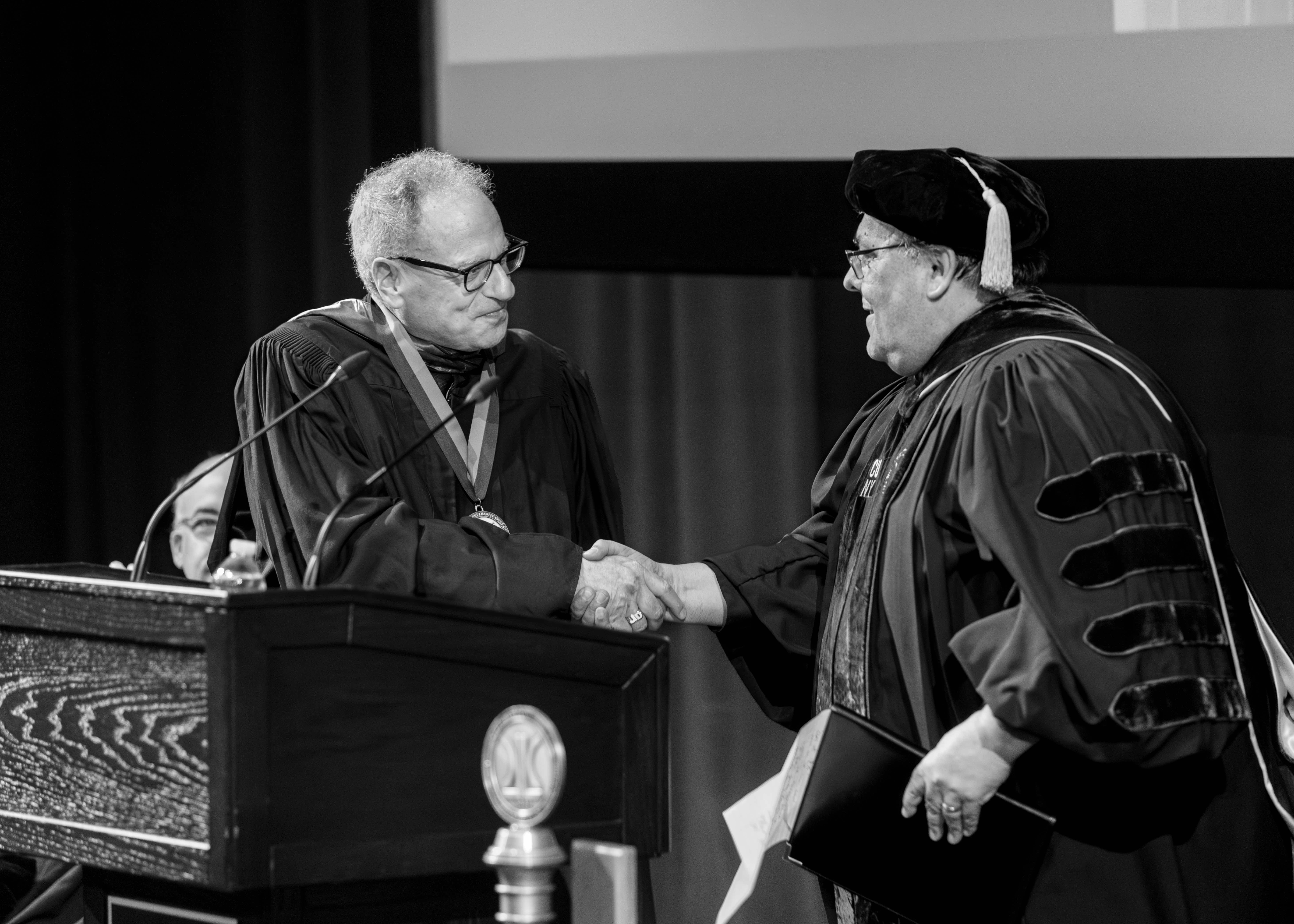 Black and white photo of President Fernando Delgado shaking hands with Jeffrey Dinowitz on stage.