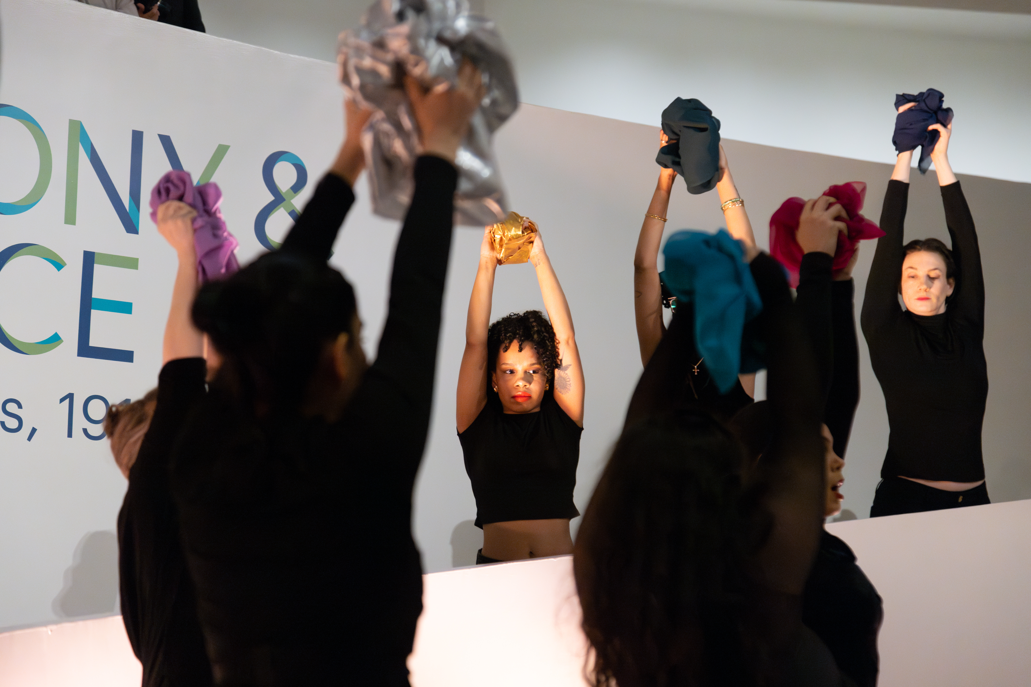 Dancers in black hold balled-up scarves over their heads.