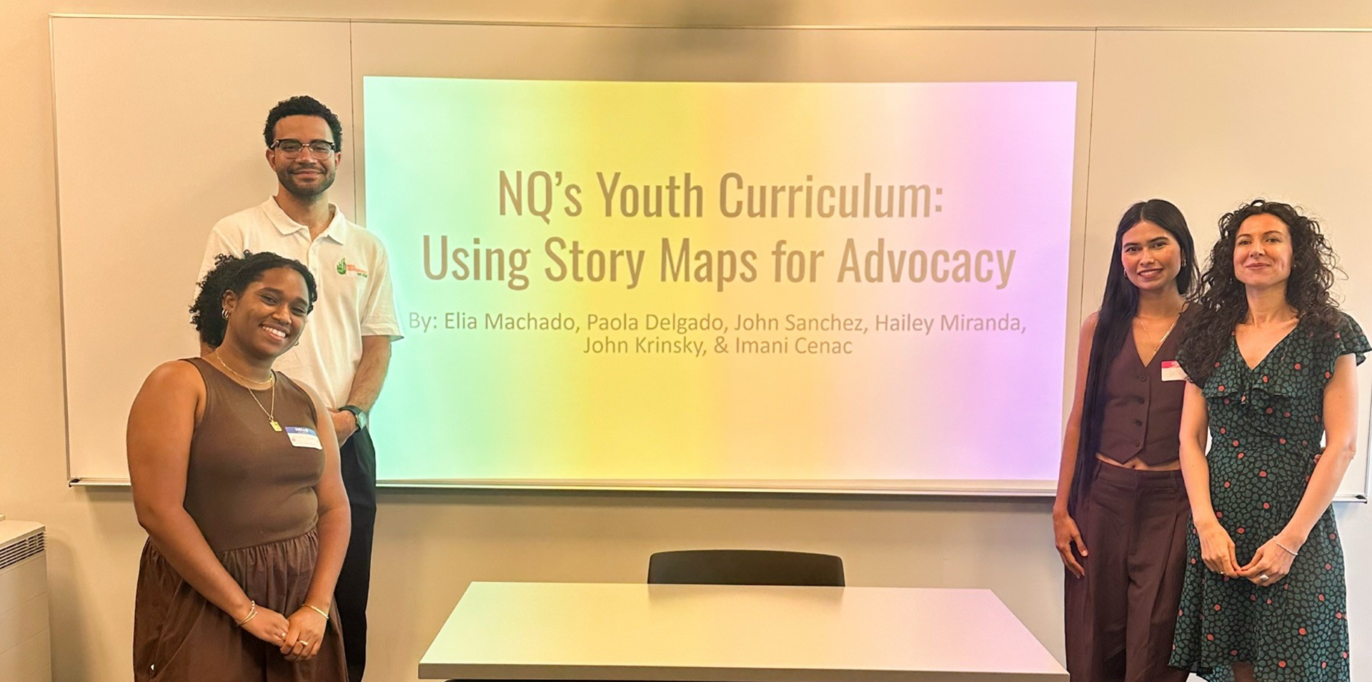four people standing in front of a presentation slide projected on a screen that reads "NQ