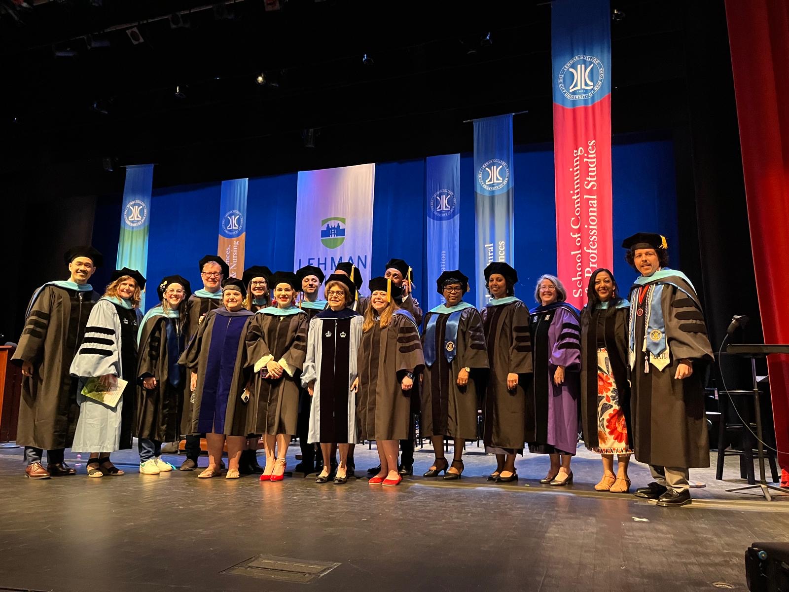 A group of graduates in regalia gathered on the stage with their advisers.