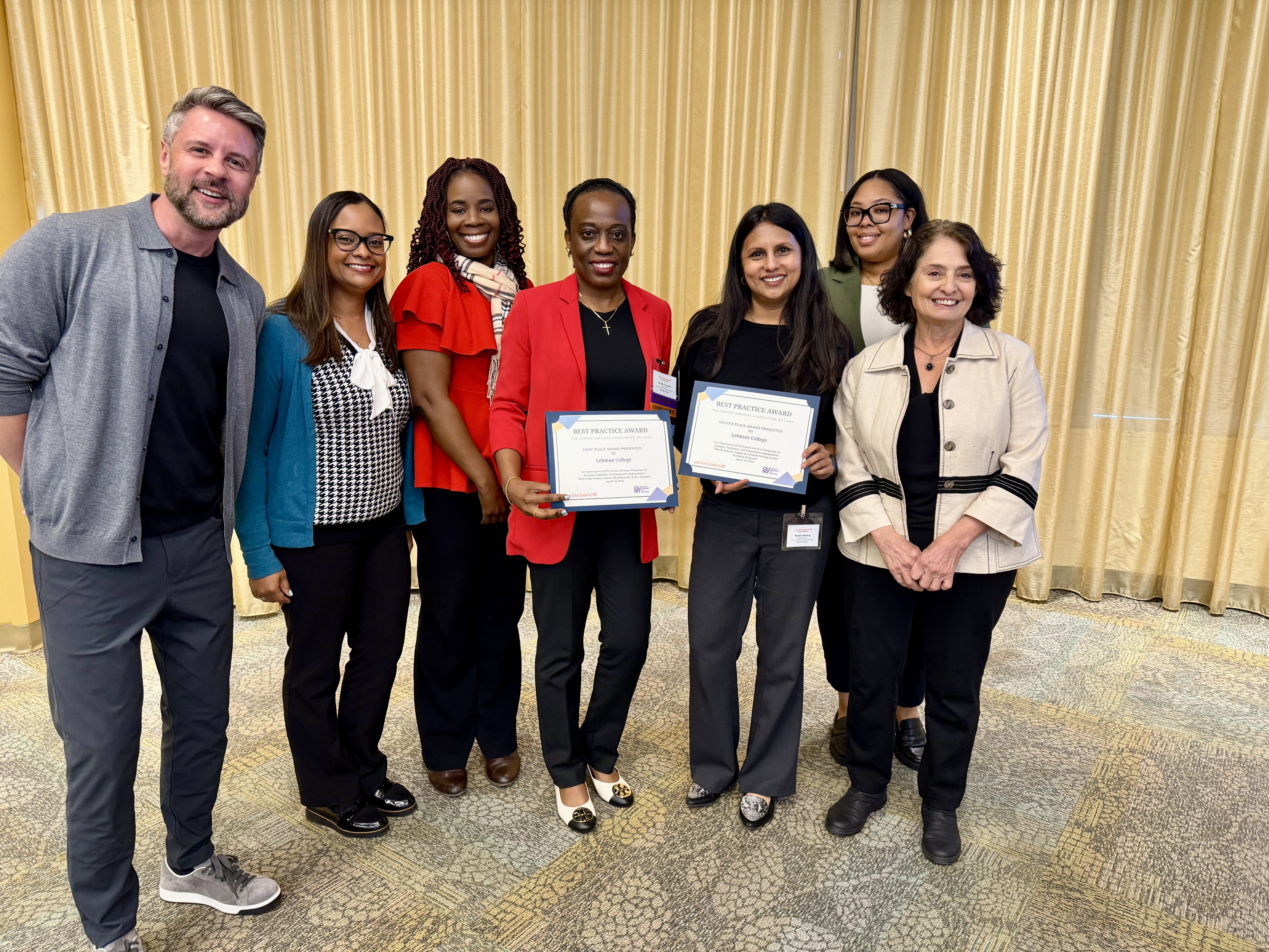 A group of people pose together, two hold certificates.