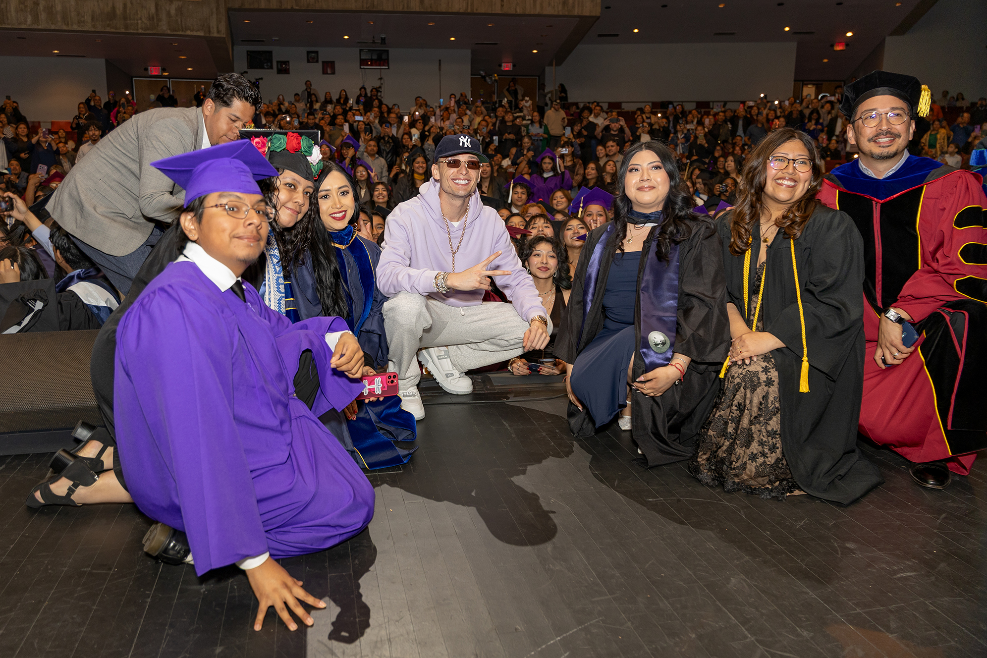 Group photo of graduating students in regalia and Peso Pluma, center