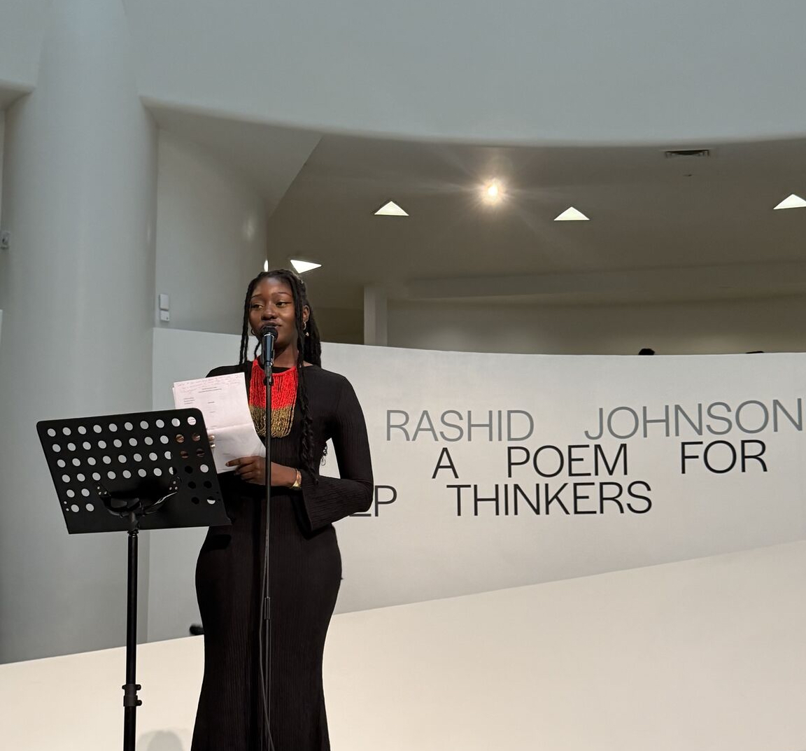 A woman reading at a podium on a stage at the Guggenheim Museum.