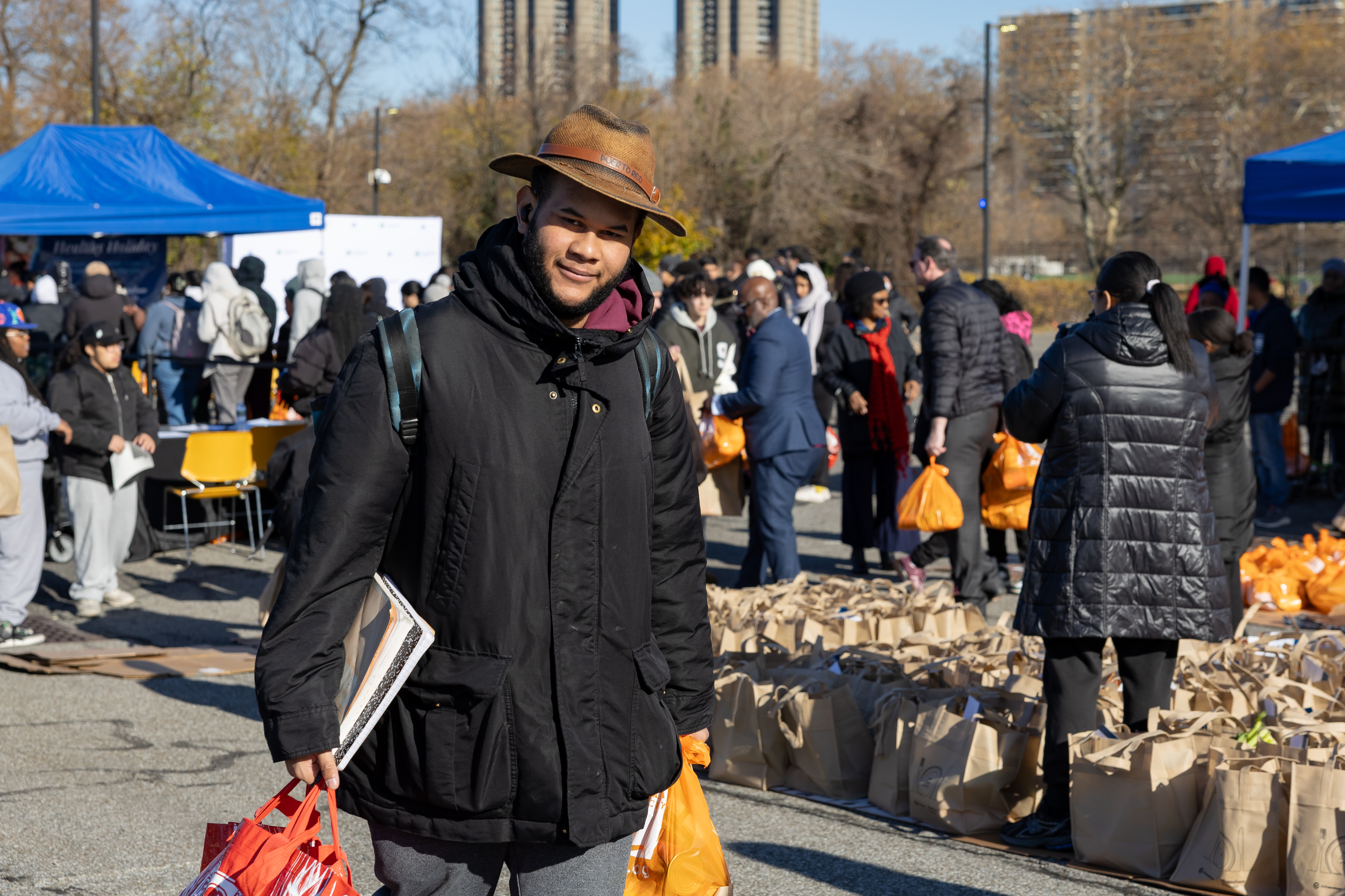 A student carrying notebooks under his arm holds two bags of food.