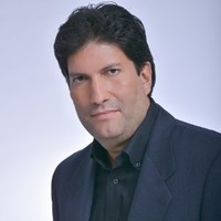 Profile pose, white man, dark hair, thin smile, wearing a dark shirt and blazer