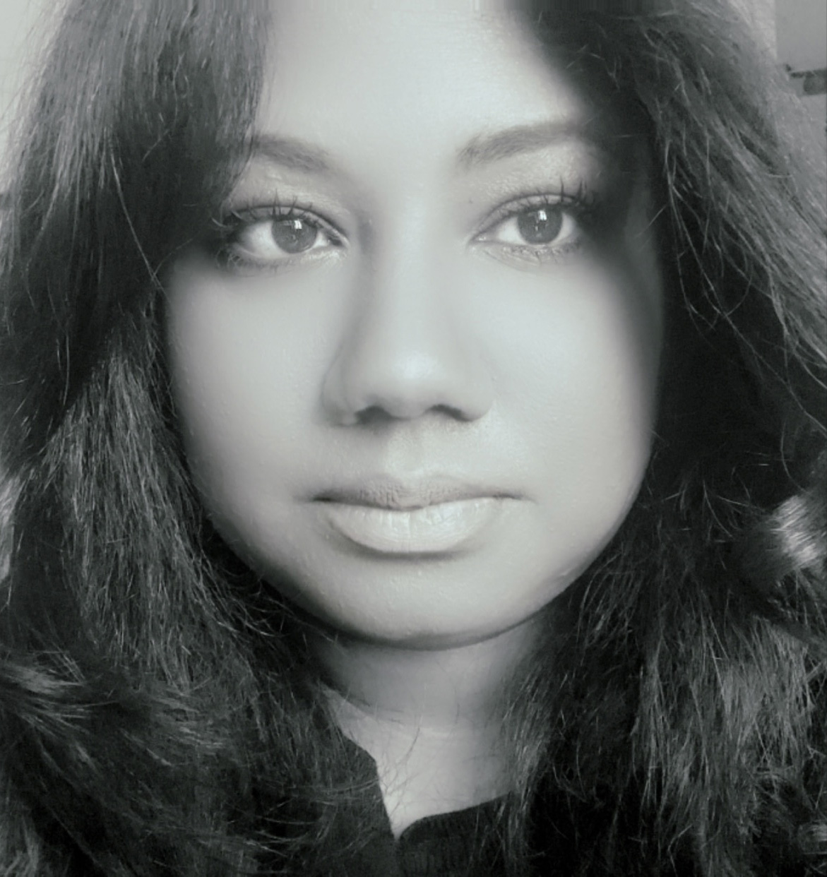 Black-and-white headshot of a person with long dark hair, looking directly at the camera with a neutral expression.